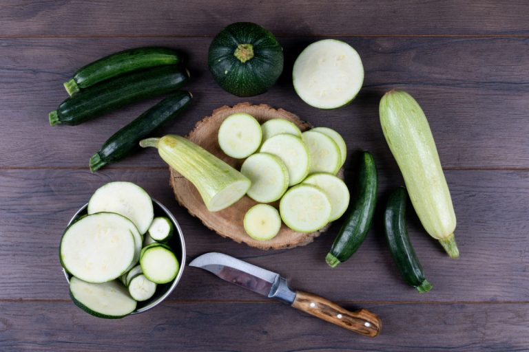 Set of knife and other zucchinis in a bowl and around and sliced zucchinis on a dark wooden background. flat lay.