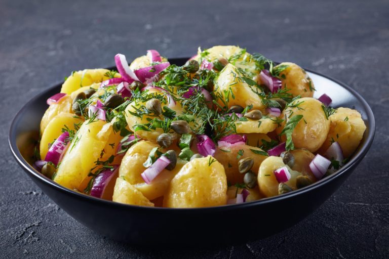 new potato salad with red onion, capers, greens in a black bowl